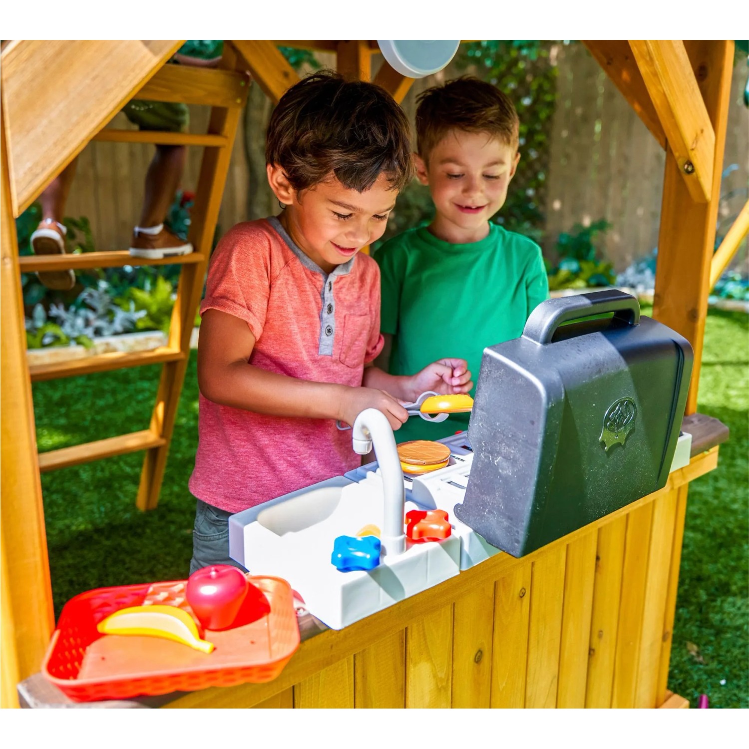 Zwei Kinder spielen in der Spielküche des Zwerkules Spielturm Bolzo mit Rutsche und Schaukel.