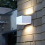 Weiße LUTEC LED-Außenwandleuchte Gemini an einer Backsteinmauer, die Licht nach oben und unten abstrahlt.