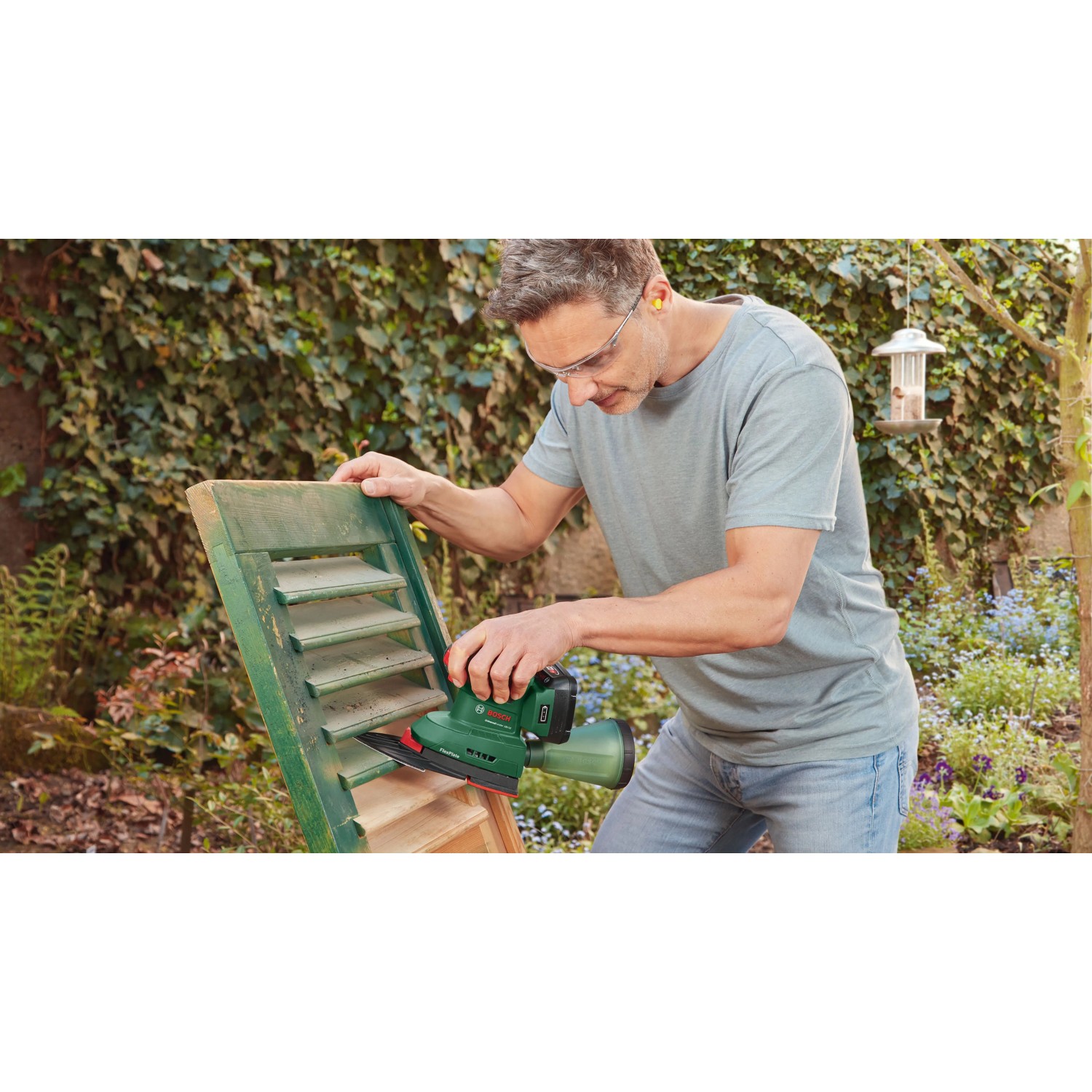 Mann schleift grüne Holzjalousie mit Bosch Akku-Multischleifer UniversalSander 18V-10. Kabelloser Deltaschleifer für vielseitige Schleifarbeiten.