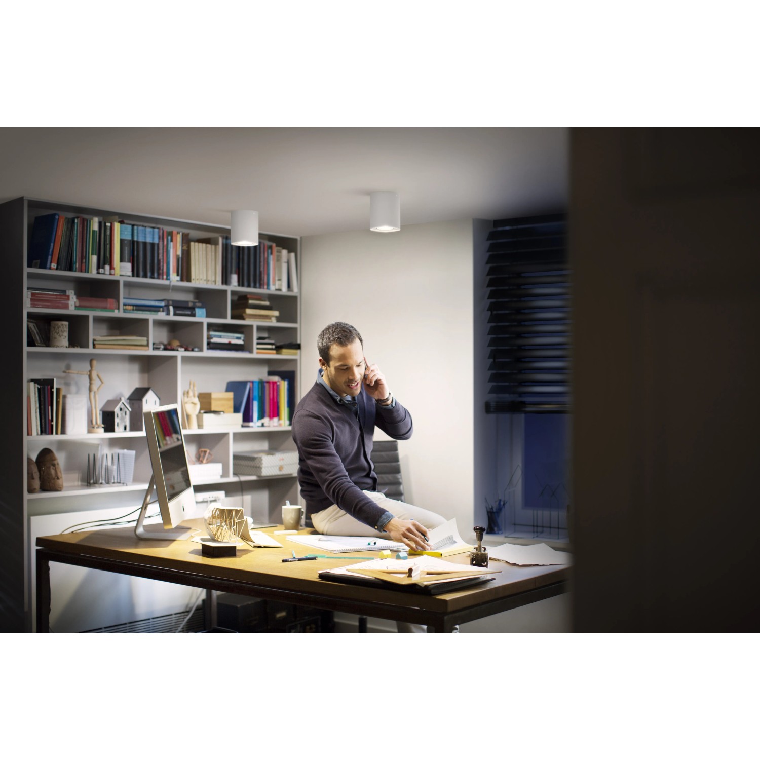 Philips Hue Pillar LED-Aufbauspot in Weiß im Wohnraum mit Mann am Schreibtisch.