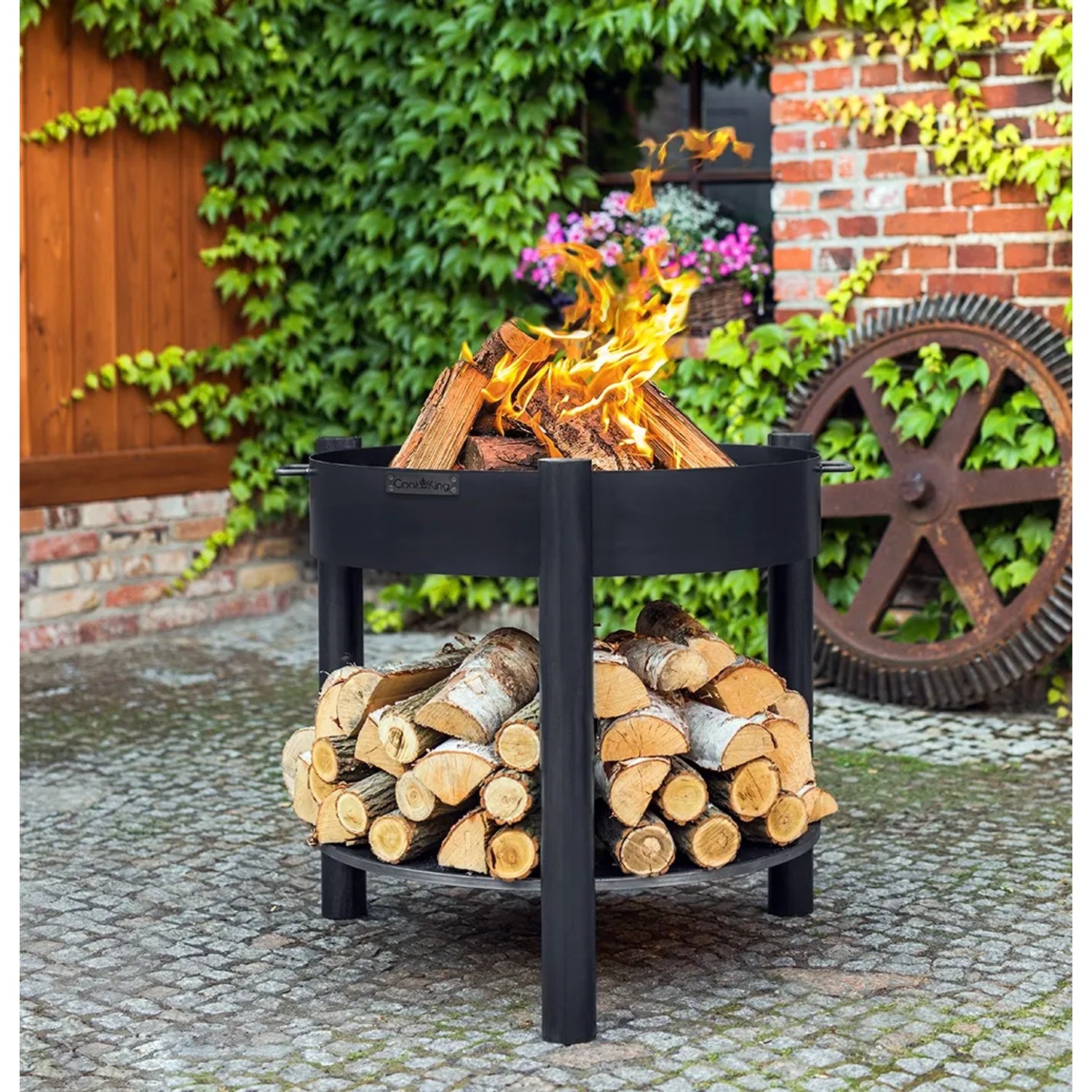 Schwarze CookKing Feuerschale Montana mit Holzlager, Ø 80 cm, mit Feuerholz befeuert.