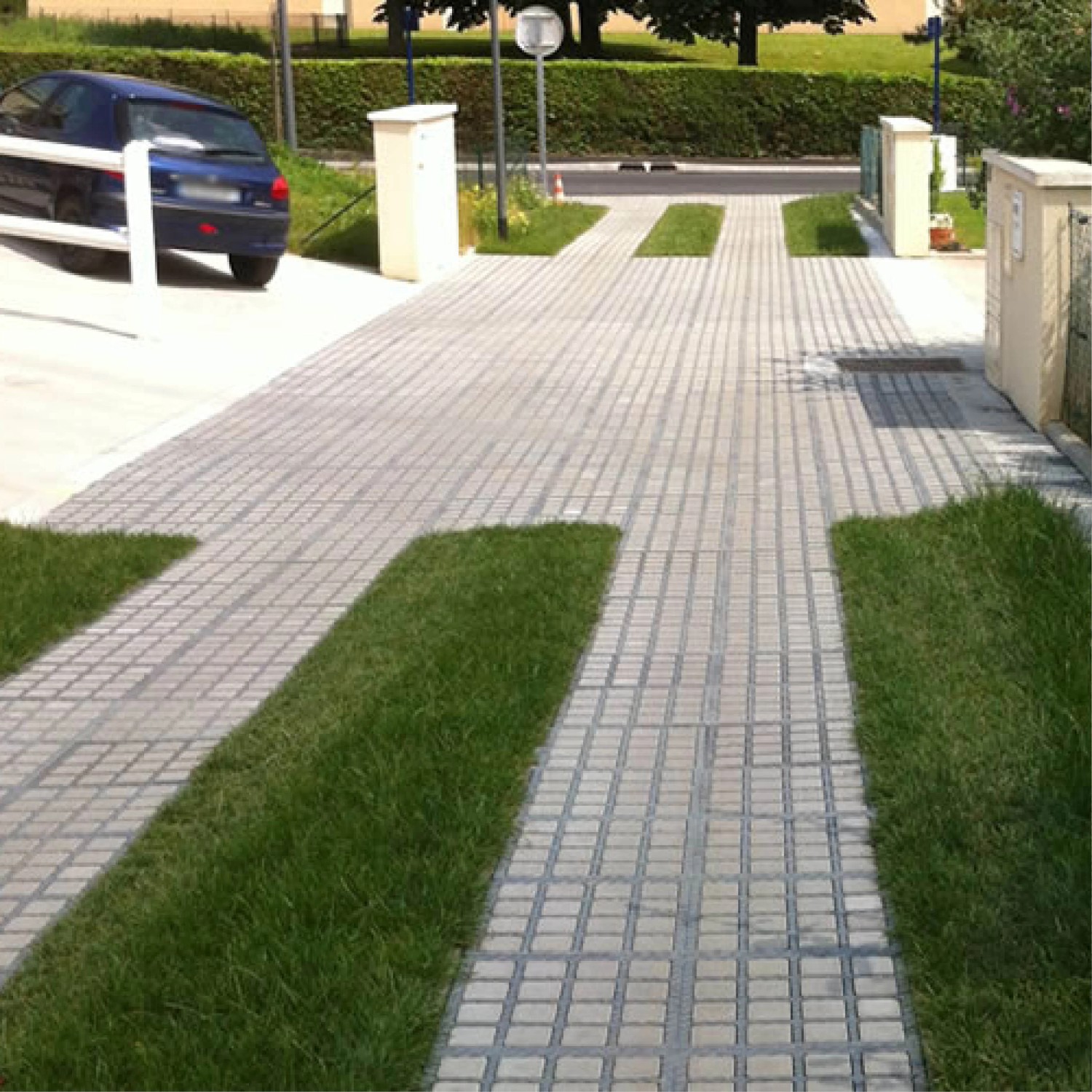 Steingraue HL Drainpflaster Füllsteine (7,4x7,4x4,9 cm) in Rasengitter auf einer Einfahrt.