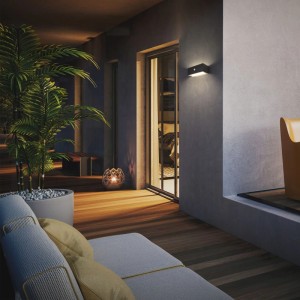 Schwarze Brilo Outdoor LED-Wandleuchte DOGU mit Akku und Bewegungssensor beleuchtet warmweiß einen Balkon.