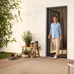 Frau geht durch Tür mit tesa® Insect Stop Lamellenvorhang in Anthrazit. Fliegengittertür für Balkon.