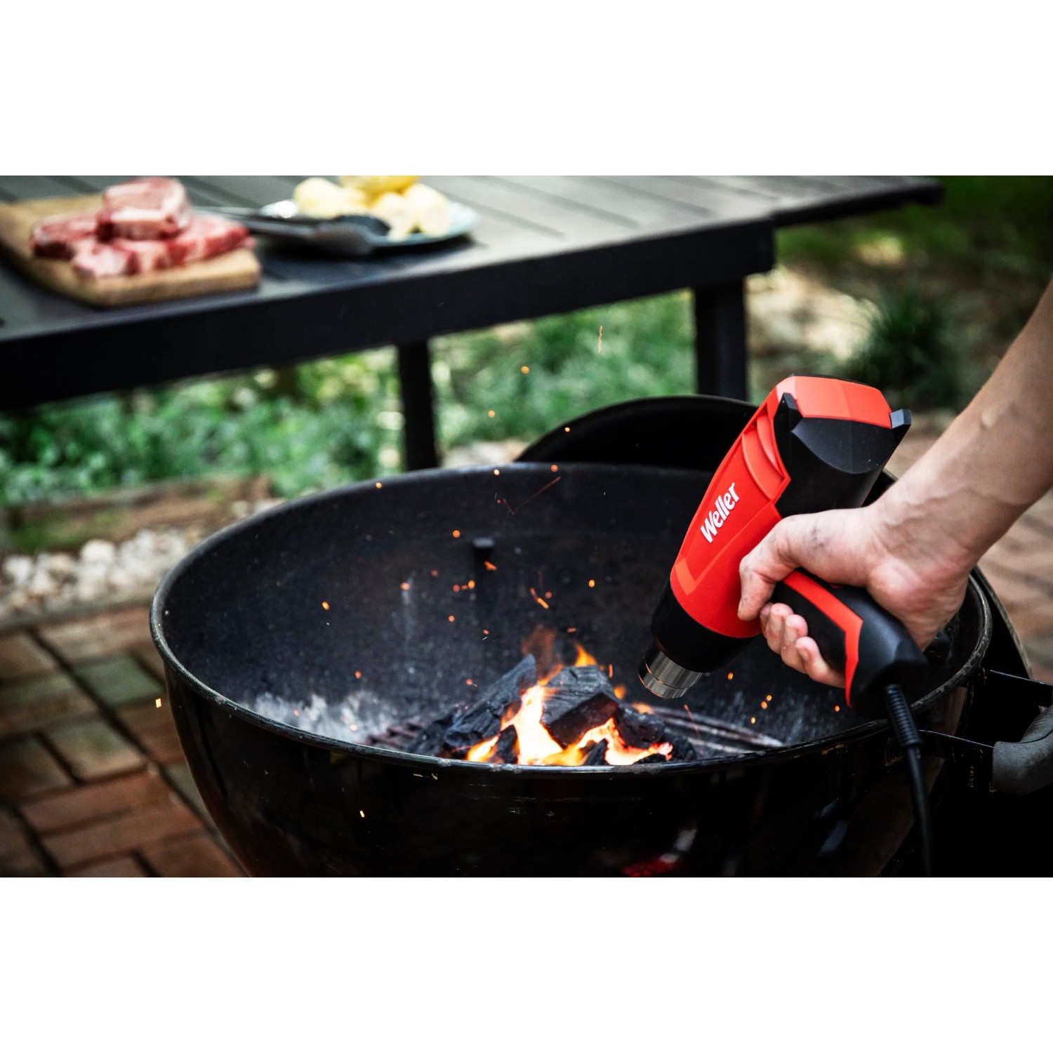 Rote Weller Heißluftpistole WLHG1623C beim Anzünden von Grillkohle.