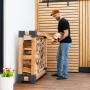 Westmann Kaminholzregal Michel aus Lärchenholz mit Holzscheiten und einer Person beim Einlagern.