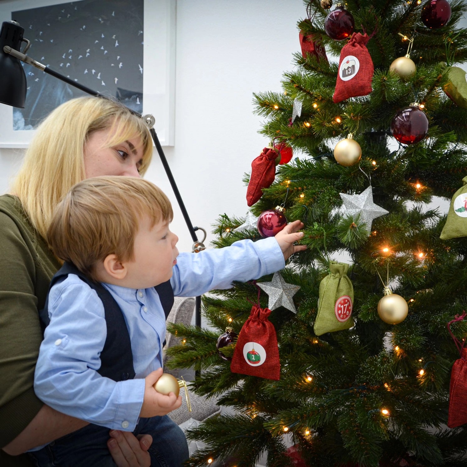DIY Adventskalender mit roten Jute-Säckchen am Weihnachtsbaum, Kind greift nach Deko.