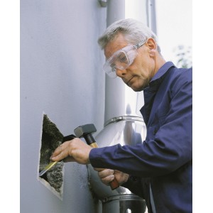 Mann trägt LUX Vollsichtbrille beim Stemmen eines Loches in eine Wand.