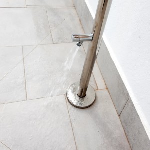 Detailaufnahme Gartendusche aus Edelstahl mit Wasserhahn und Wasserfluss.