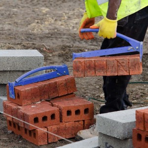 Blaue Wiltec Ziegelzange hebt rote Ziegelsteine. Robuster Steinheber für effizienten Transport auf Baustelle.