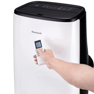 Weiße Honeywell mobile Klimaanlage mit schwarzem Bedienfeld. Eine Hand bedient die Fernbedienung, die 22°C anzeigt.