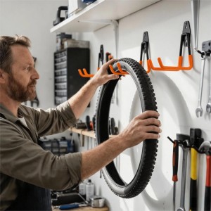 Mann hängt Fahrradreifen an orange-schwarzen Wandhaken in Werkstatt. Relaxdays 12-teiliges Set für Garage & Ordnung.