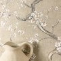 Beige Vliestapete mit weißen Kirschblüten und Ästen, ein Krug im Vordergrund. Dekorative Blumentapete für Wohnräume.