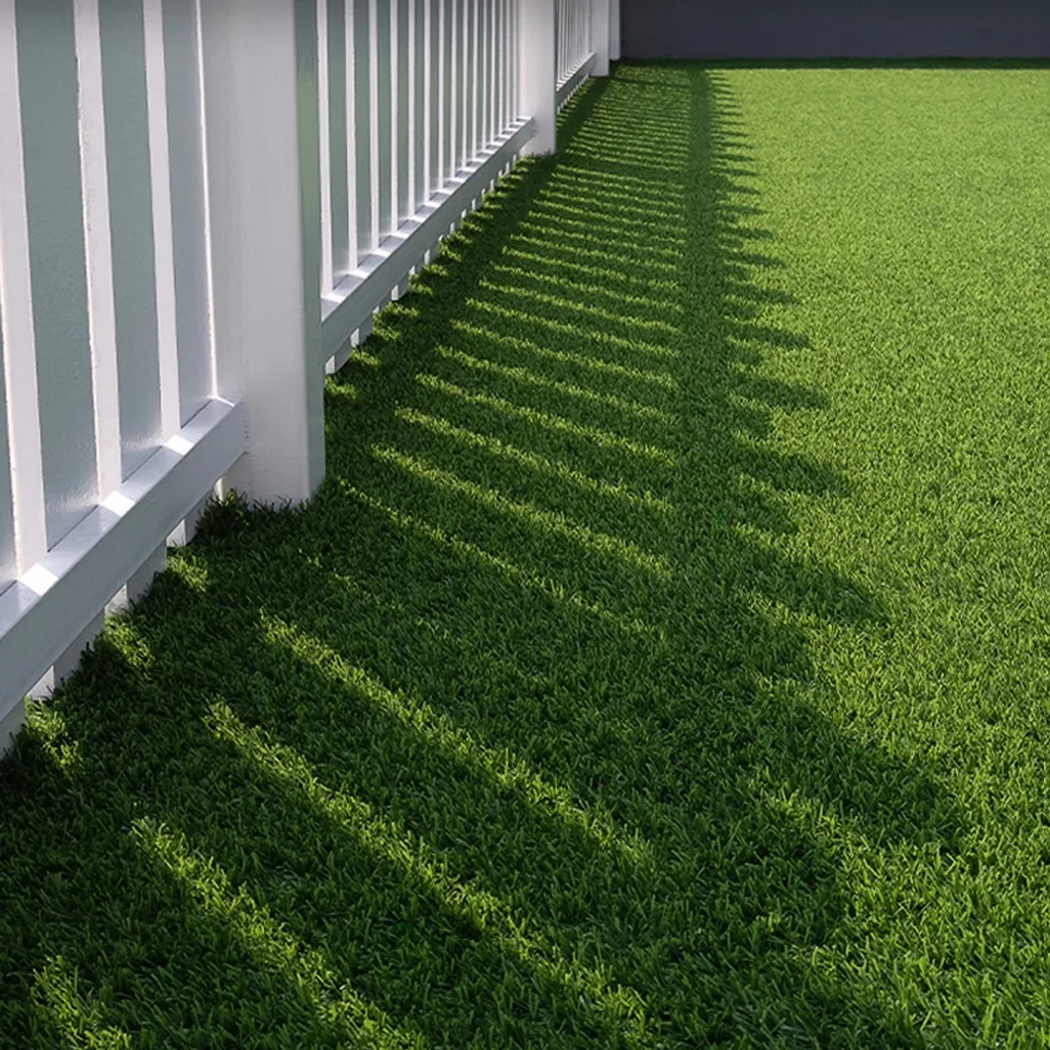 Detailaufnahme: Grüner Primaflor Kunstrasen Arizona neben weißem Zaun.