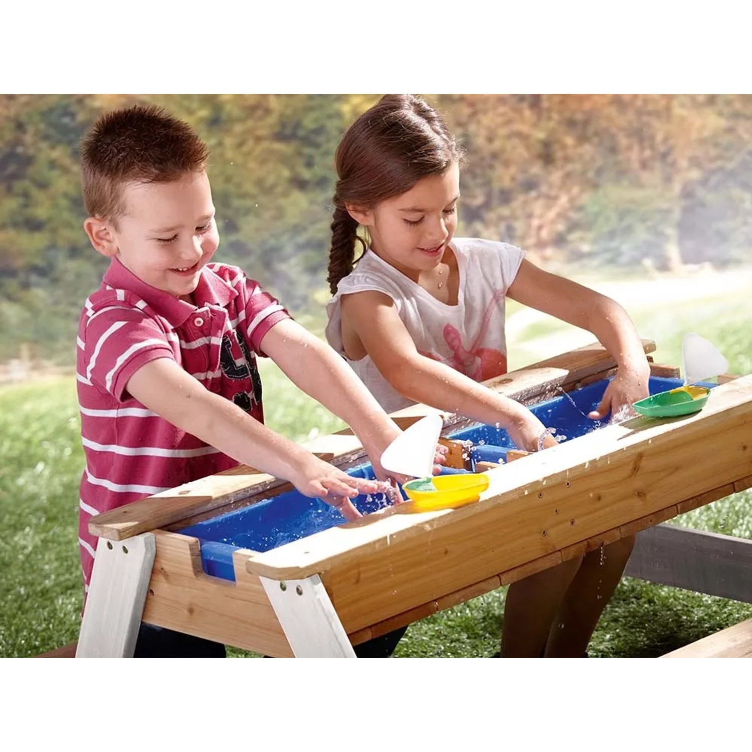 Kinder spielen am Axi Nick Sand- und Wasser-Picknicktisch aus Holz mit Sonnenschirm.