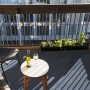 Graublauer Primaflor Rasenteppich auf Balkon mit Tisch, Stuhl und Pflanzen.