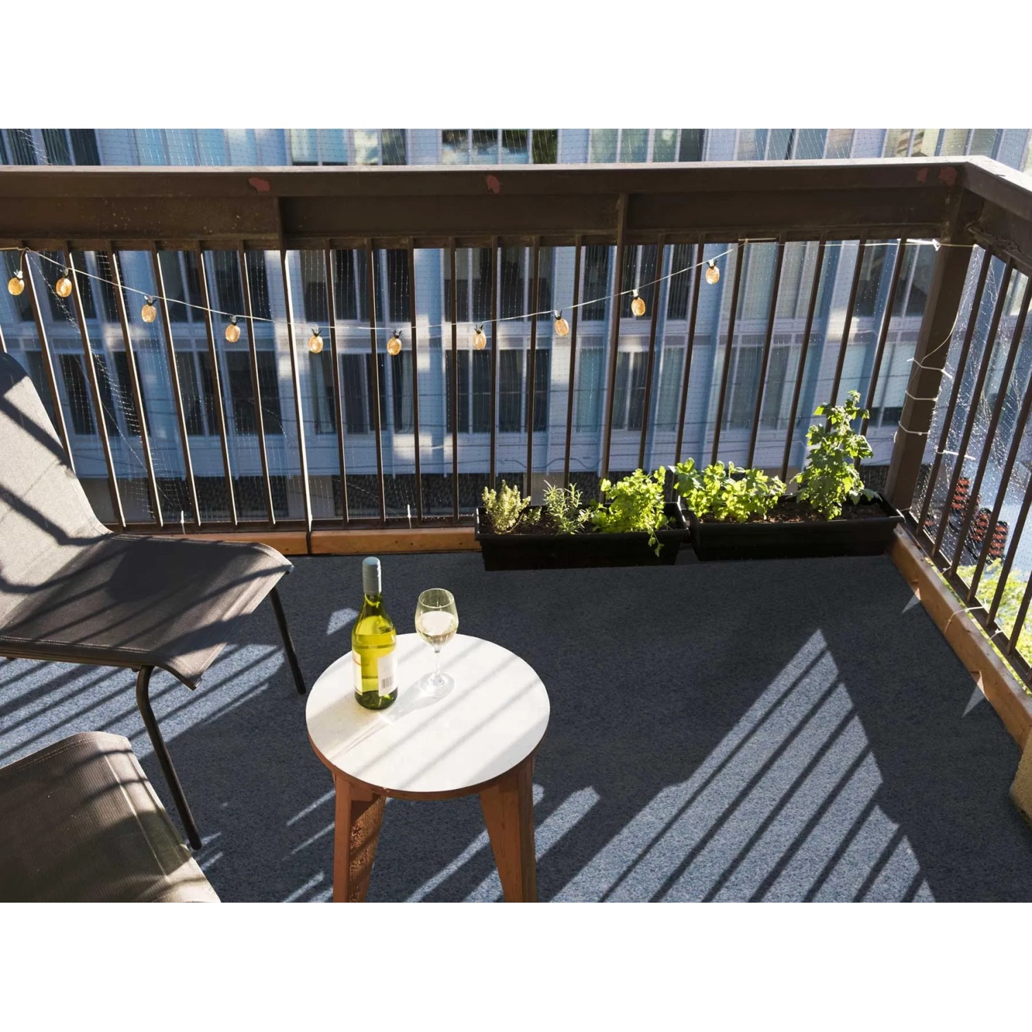 Graublauer Primaflor Rasenteppich auf Balkon mit Tisch, Stuhl und Pflanzen.