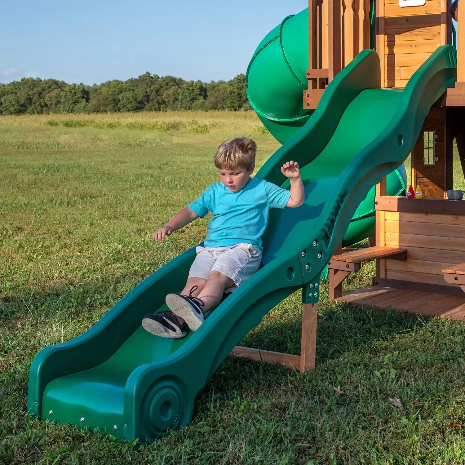 Kind rutscht grüne Rutsche am Backyard Discovery Spielturm Cedar Cove hinunter.