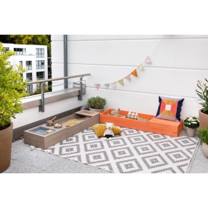 MUDDY BUDDY Sandkasten Flexy Style in Warmgrau und Lachs mit Spielzeug auf einem Balkon.