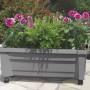 Grauer KHW Pflanzkasten Calypso mit Bewässerungssystem und Rollen, bepflanzt mit Blumen und Farn.
