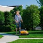 Frau vertikutiert Rasen mit gelbem Stiga Elektro-Vertikutierer SV 213 E. Rasenpflege im Garten.