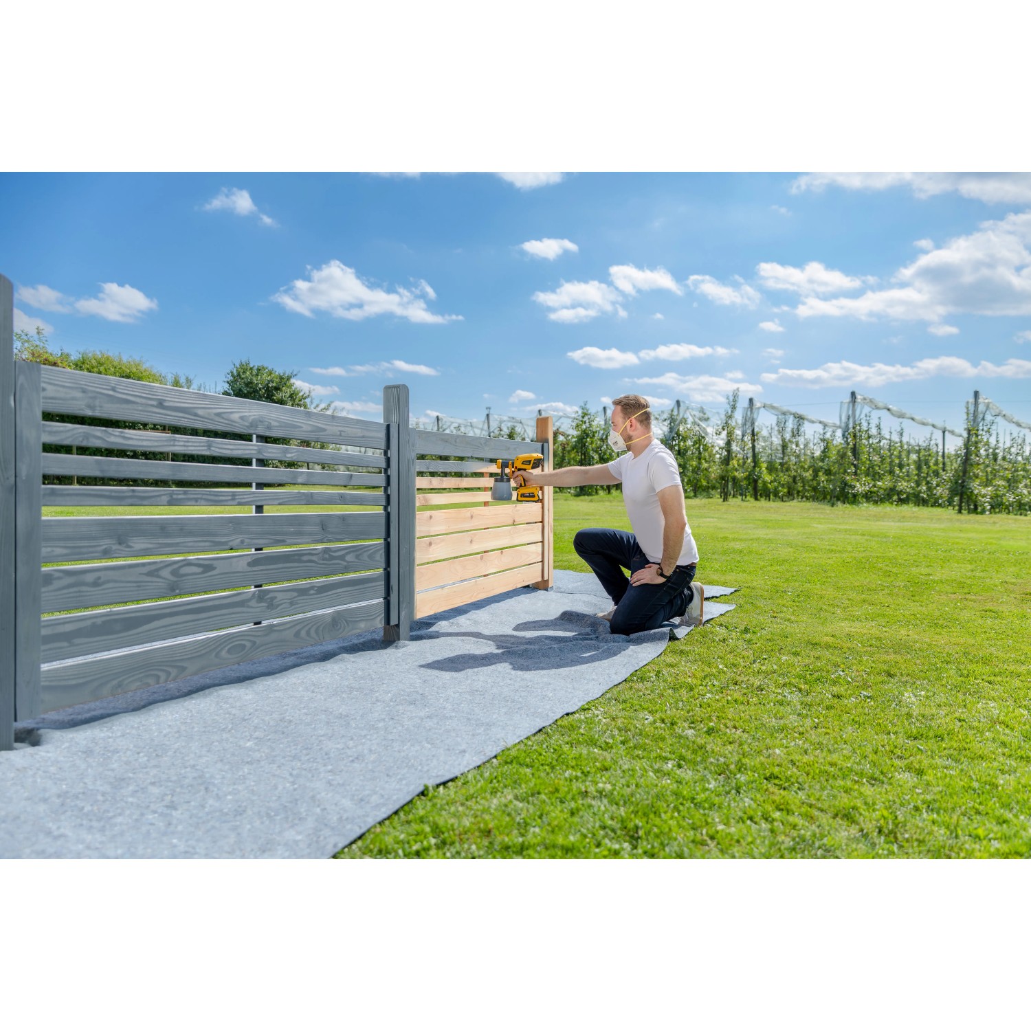 Mann sprüht mit Wagner Akku-Farbsprühsystem W 600 FLEXiO einen Holzzaun im Garten.