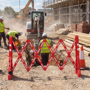 Rotes, ausziehbares Absperrgitter mit weißen Reflektorstreifen sichert Baustelle mit Arbeitern und Graben. Schutzgitter.