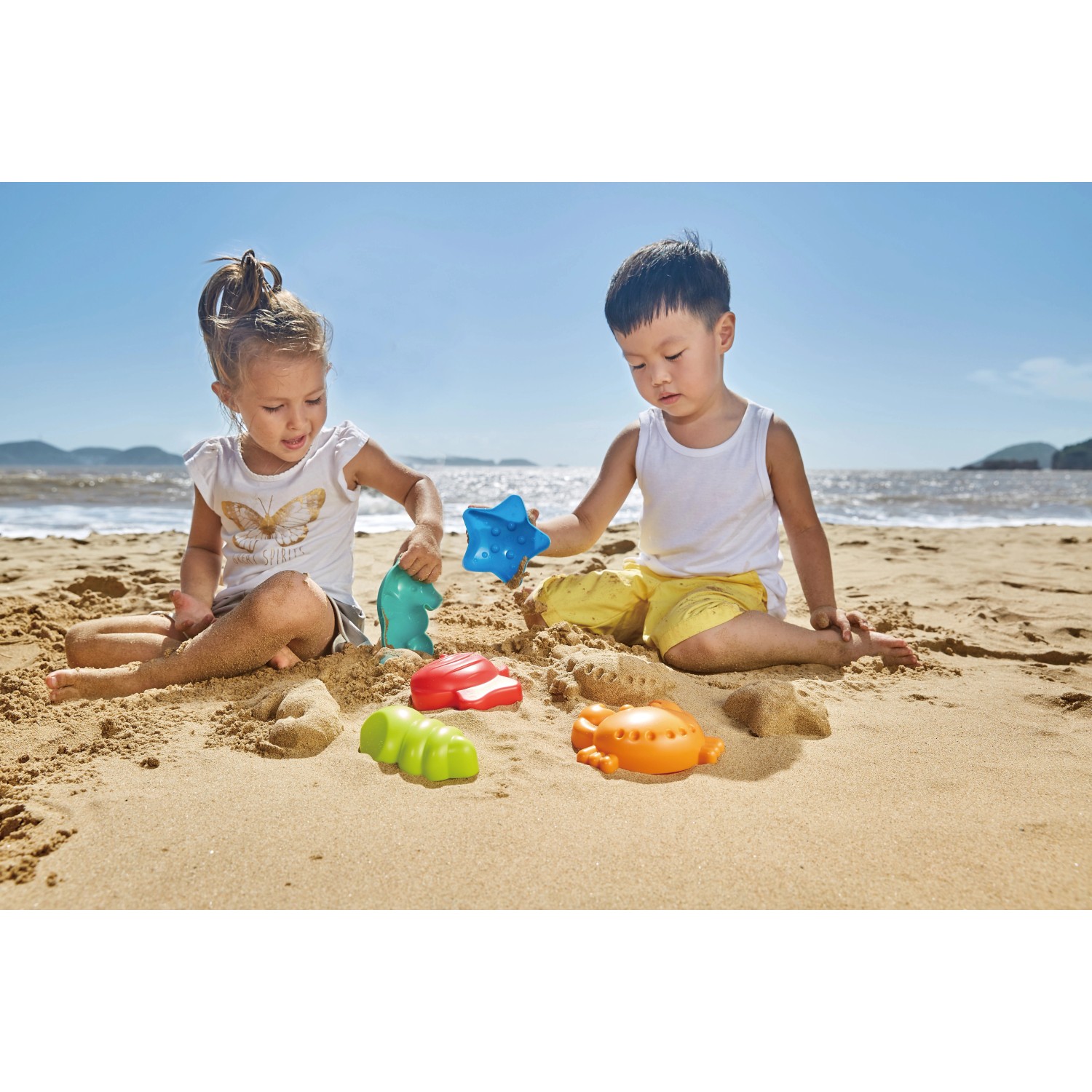 Kinder spielen mit Hape Sandspielzeug Meerestier-Förmchen (5-teilig) am Strand.
