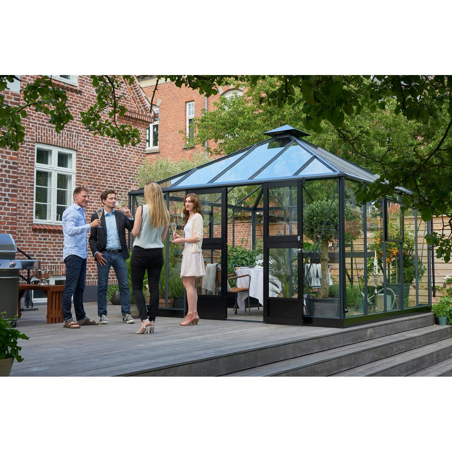 Juliana Gewächshaus Oase 13 Anthrazit mit Personen im Garten. Begehbares Glas-Gewächshaus mit Aluminiumrahmen.