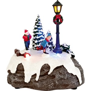 Weihnachtsdorf Figur mit beleuchteter Laterne, Eisläufern und Tannenbäumen auf Schnee. Mehrfarbige Weihnachtsdekoration aus Kunststoff.