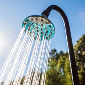 Gre Solardusche Holzoptik mit Wasserstrahl vor blauem Himmel und Bäumen.