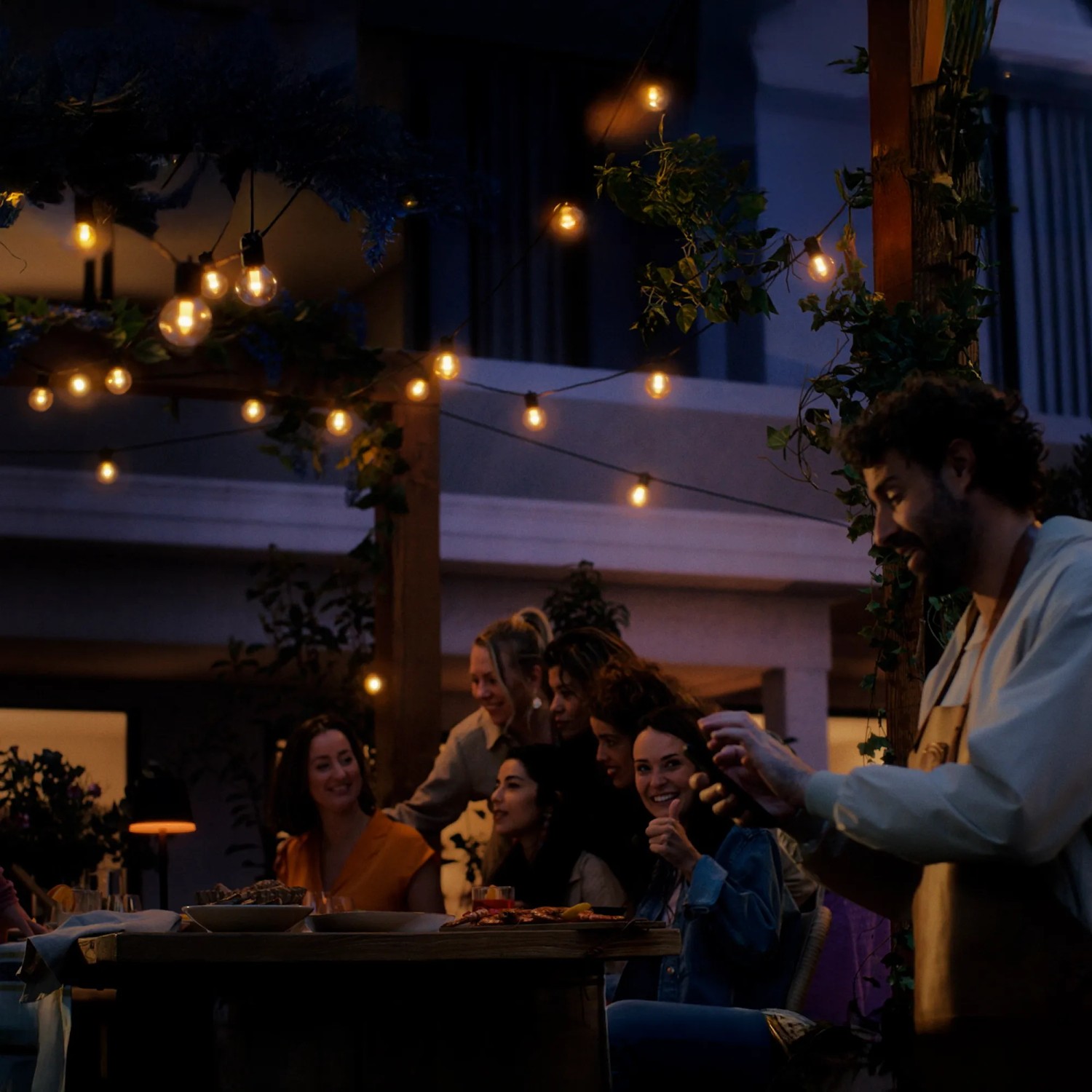 Gruppe feiert unter der Philips Hue Festavia Lichterkette mit warmem Licht im Garten.