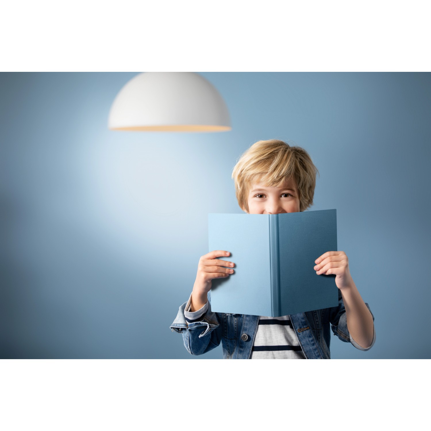 Philips LED E27 Leuchtmittel in Glühlampenform, neutralweißes Licht, unter einer weißen Lampe liest ein Kind ein Buch.