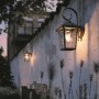 Schwarze Philips Buzzard Außenwandleuchte im Vintage-Stil leuchtet warm an einer Gartenmauer. Stimmungsvolle Beleuchtung.