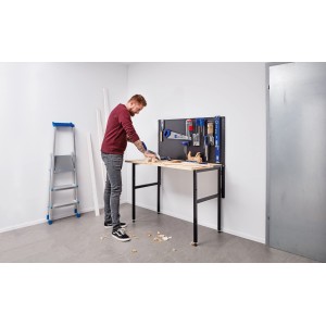 Klappbare Werkbank (120 cm) mit Werkzeugwand und Handwerker beim Sägen von Holz.