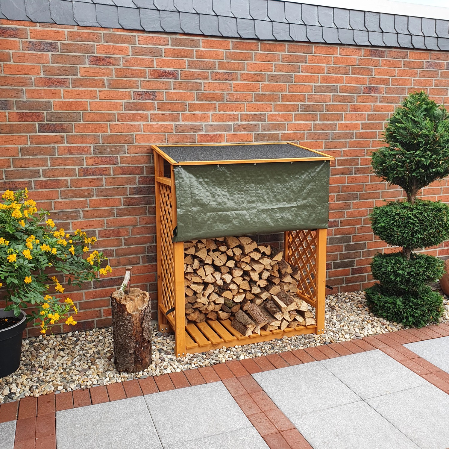 Honigbraunes Kaminholzregal Speyer mit Wetterschutzplane und Holzscheiten vor einer Ziegelwand.