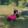 Mädchen befüllt pinke Pro-Bau-Tec Kinderschubkarre (20 l) mit Holz im Garten.