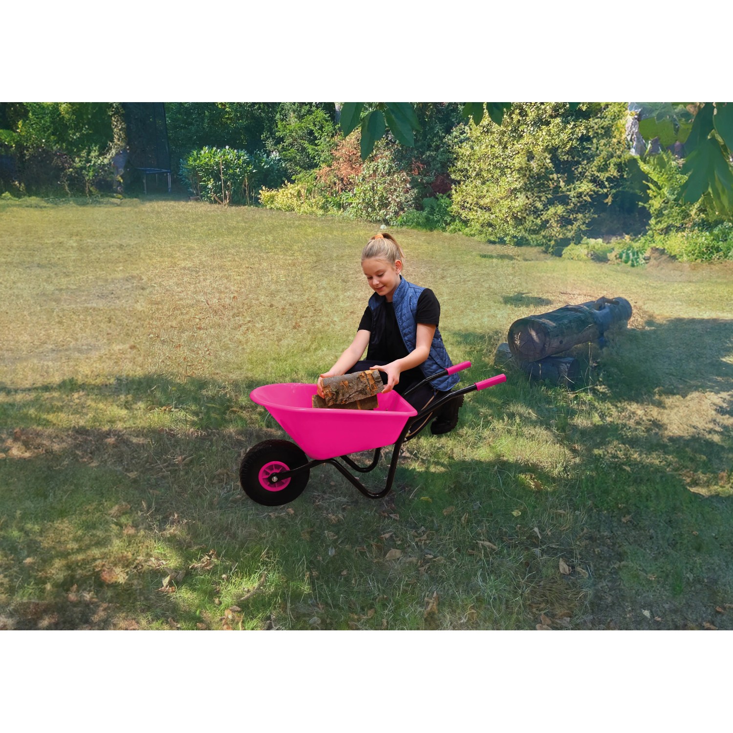 Mädchen befüllt pinke Pro-Bau-Tec Kinderschubkarre (20 l) mit Holz im Garten.