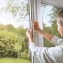 Frau montiert anthrazitfarbenes Tesa Pollenschutzgitter am Fenster.