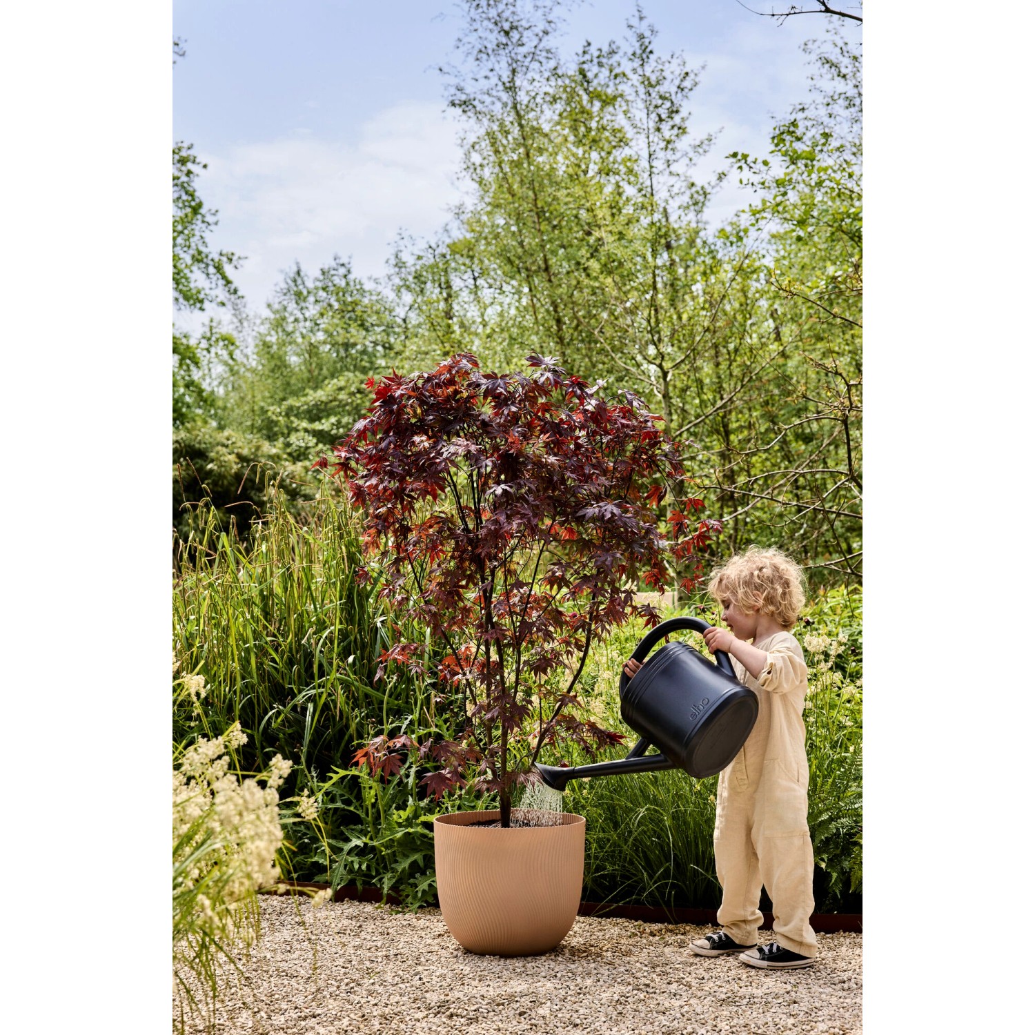 Brauner Elho Blumentopf Sereh (Ø 47 cm) mit Kind beim Gießen einer Pflanze im Garten.