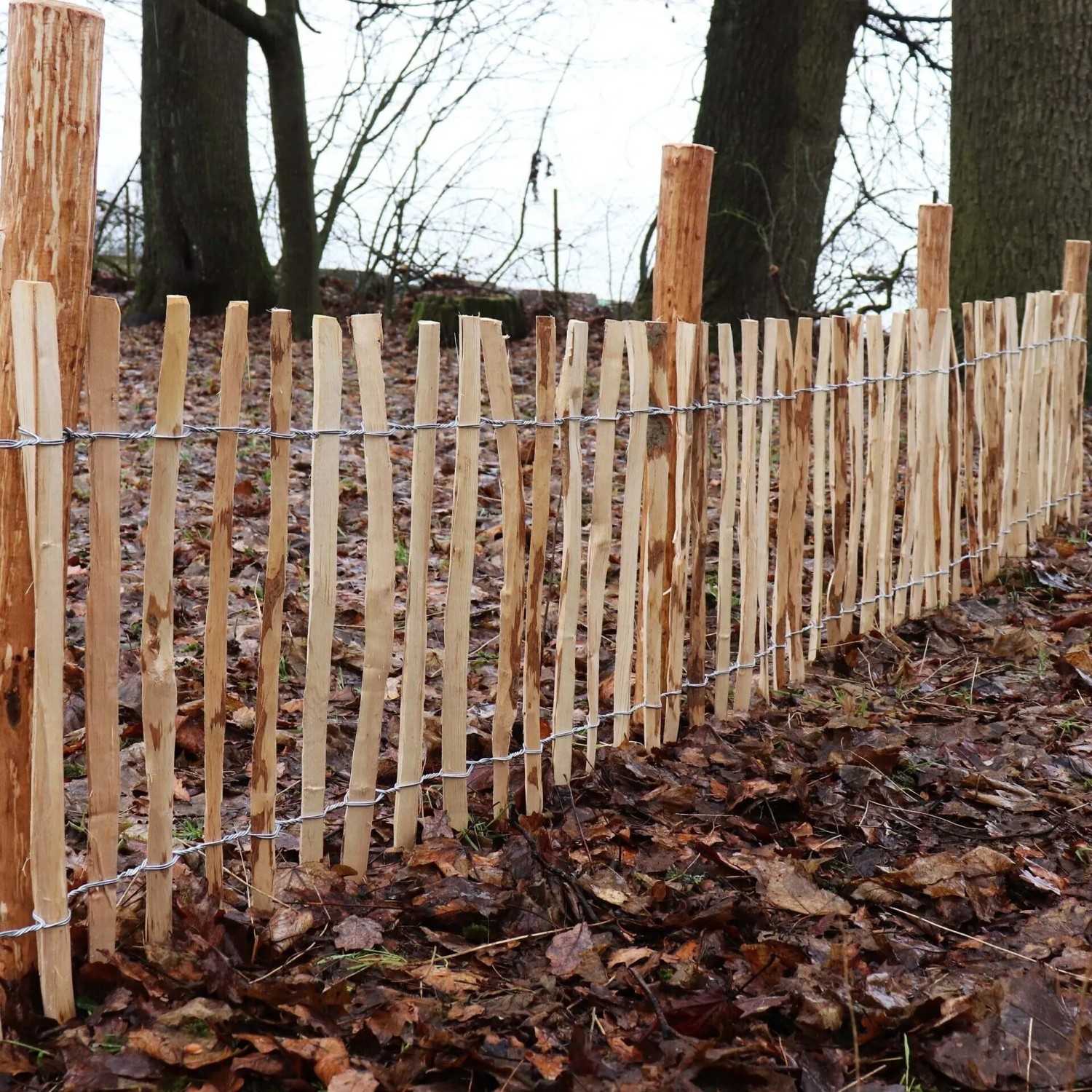 Staketenzaun aus Haselnuss mit Holzpfosten (1,5m, Ø 6-9cm) im Garten.