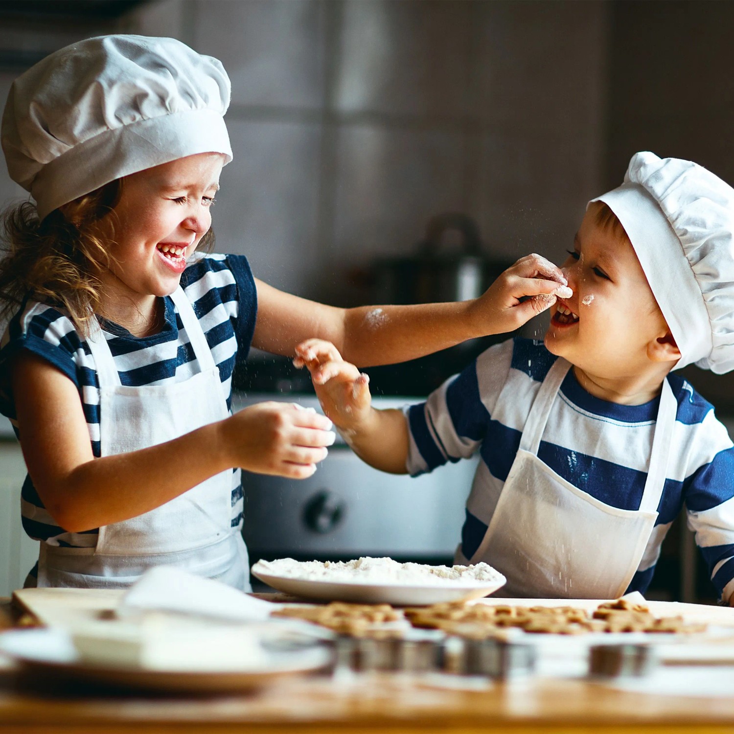 Fröhliche Kinder in Kochmützen backen Plätzchen und spielen mit Mehl. Eine Schüssel Mehl steht auf dem Holztisch.
