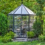 Sechseckiges Palram Canopia Oasis Gewächshaus (2.5x2.1m) mit Doppeltür und Lamellenfenster im Garten.