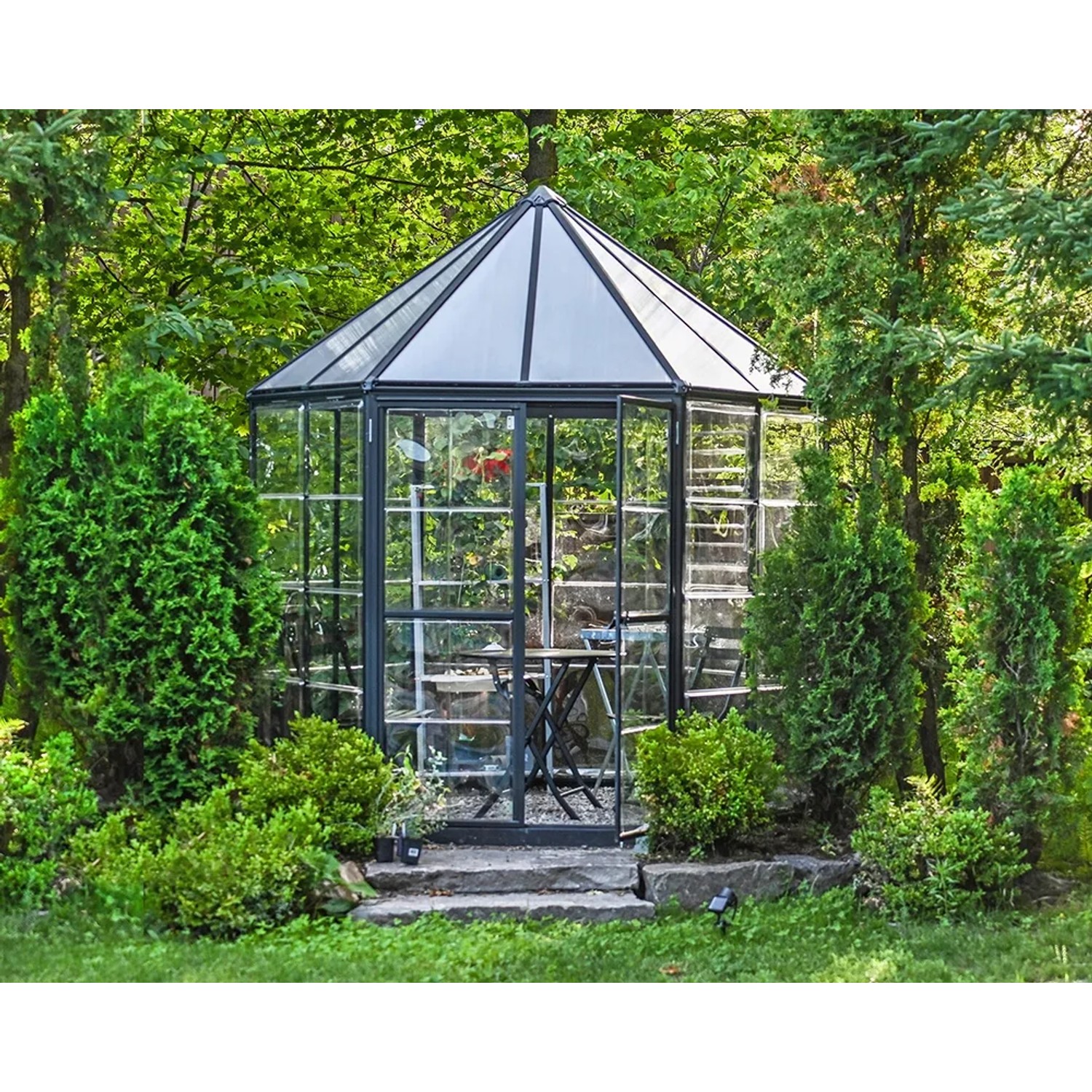Sechseckiges Palram Canopia Oasis Gewächshaus (2.5x2.1m) mit Doppeltür und Lamellenfenster im Garten.
