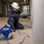 Blaue Garant Kabeltrommel 25m IP44 auf Baustelle, Arbeiter bohrt in Wand. Ideal für Gewerbe & Outdoor.