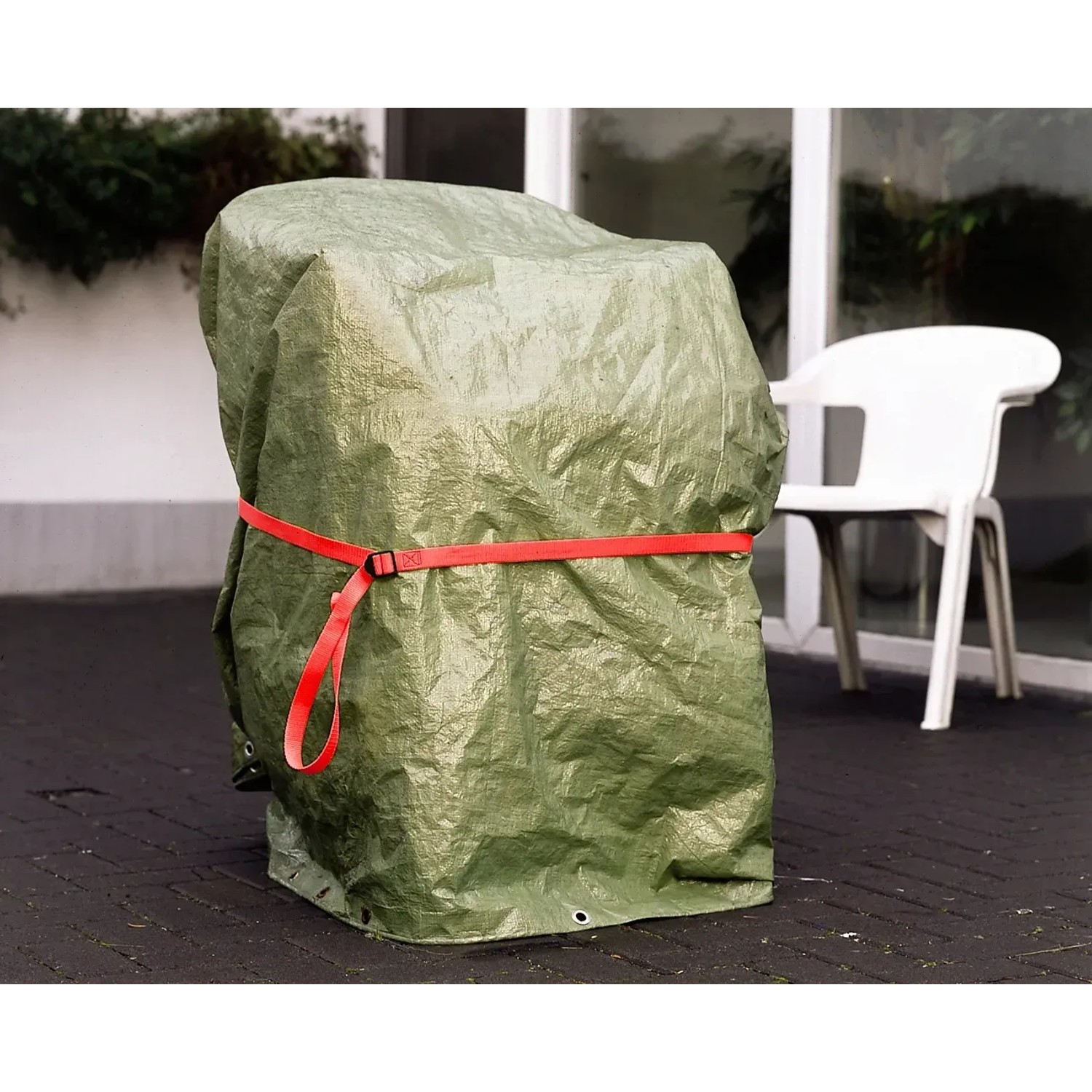 Abgedeckter Gegenstand mit rotem Gurt (25 mm, 2,5 m). Spanngurt zur Sicherung von Gartenmöbeln.