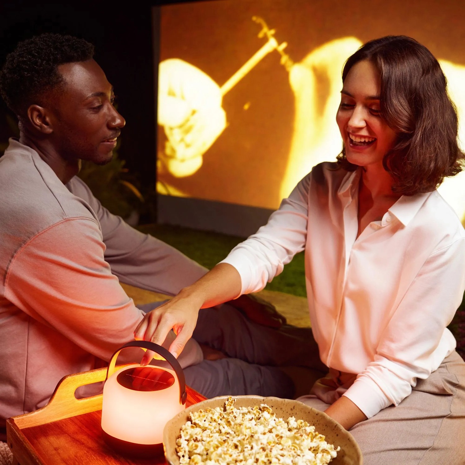 Szene mit Philips Solarleuchte Alula: Paar genießt Filmabend im Freien mit LED-Tischleuchte.