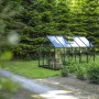 Schwarzes Halls Gewächshaus Popular 106 mit 6,2 m² im Garten, umgeben von Grün.