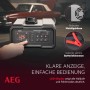 AEG Batterieladegerät CW10 mit LED-Display und Batterieklemmen vor Oldtimer. Autoelektrik Zubehör.