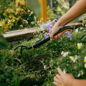 Fiskars Kleingrubber im Einsatz: Handgrubber mit orange-schwarzem Griff lockert Erde im Gartenbeet.